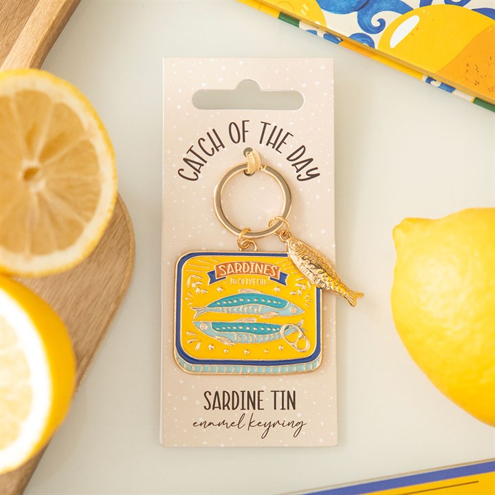 Sardine tin enamel keyring lifestyle shot on Catch of the Day backing card with fresh lemon slices and blue tile background