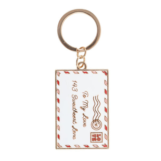 Love letter enamel keyring charm close up on white background showing white envelope with red airmail border and gold postmark