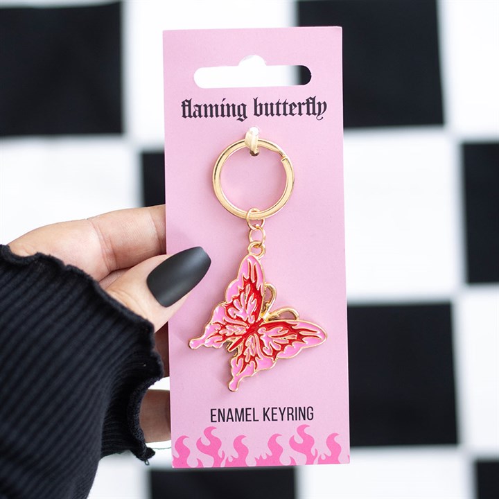 Flaming butterfly enamel keyring lifestyle shot held in hand against black and white checkerboard background on hot pink backing card